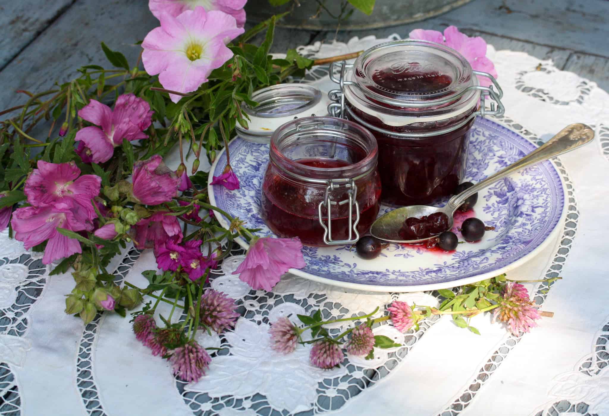 Krusbärssylt i burkar på en lila antik tallrik och omgiven lila blommor.